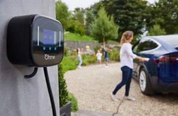 Ohme Motable EV Charger fitted on a driveway with woman plugging it into her blue car. 3 young children playing in the background.