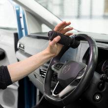 A driver's seat view of the steering wheel. The driver is holding the wheel via the BraunAbility 2-Pin Specialist Steering Aid. It is a soft foam handle perpendicular to the wheel with a supportive pin to hold the hand in place.