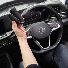 A driver's seat view of the steering wheel. The driver is holding the quick-release specialist steering aid the BraunAbility 2-Pin Specialist Steering Aid. It is a soft foam handle perpendicular to the wheel with a supportive pin to hold the hand in place.