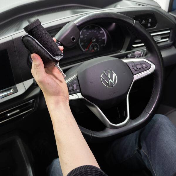 A driver's seat view of the steering wheel. The driver is holding the quick-release specialist steering aid the BraunAbility 2-Pin Specialist Steering Aid. It is a soft foam handle perpendicular to the wheel with a supportive pin to hold the hand in place.