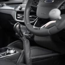 A driver's seat view of the Carospeed Classic, a floor-mounted mechanical push/pull accelerator and brake. A tall black handle with a button on the side to hold the brake. It is positioned for the driver's left hand beside the centre console.