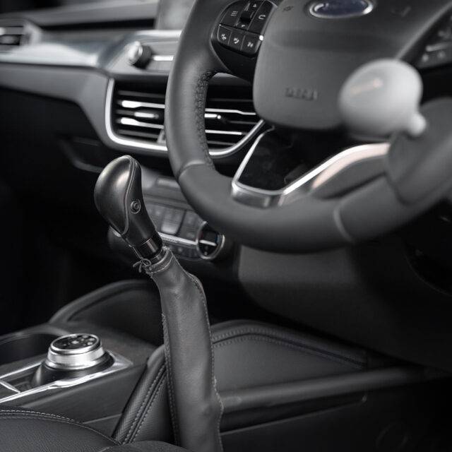 A driver's seat view of the Carospeed Classic, a floor-mounted mechanical push/pull accelerator and brake. A tall black handle with a button on the side to hold the brake. It is positioned for the driver's left hand beside the centre console.