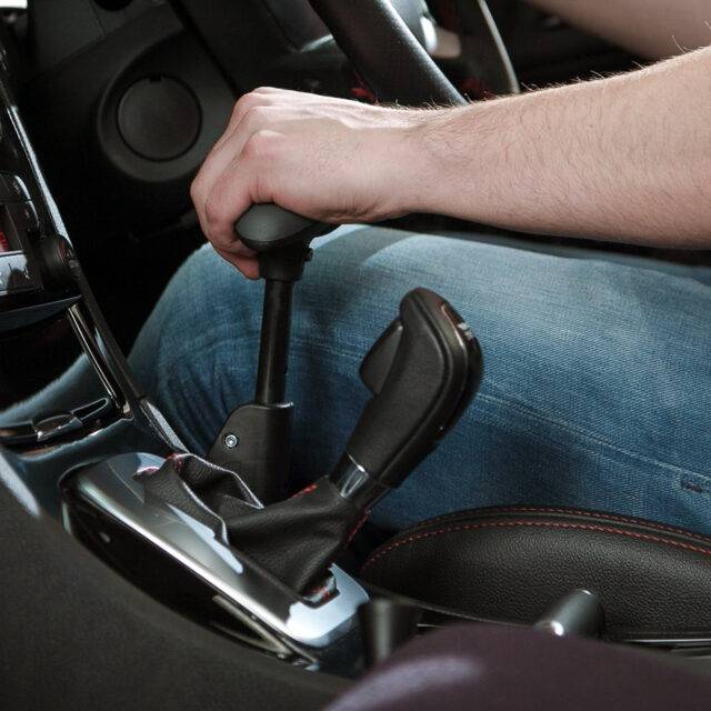 A view of a driver holding the BraunAbility Carospeed Menox hand control, a sleek black twist & push handle hand control for accelerating and braking their car.