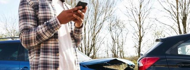 Zoomed in image of man holding his phone contacting Motability insurance, with image of a vehicle broken down behind him.
