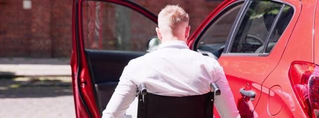 Male wheelchair user transferring into a red car