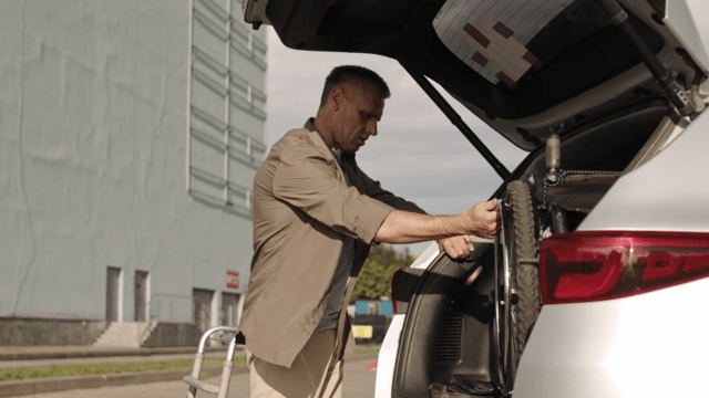 man struggling to lift a wheelchair out of the boot of a silver car