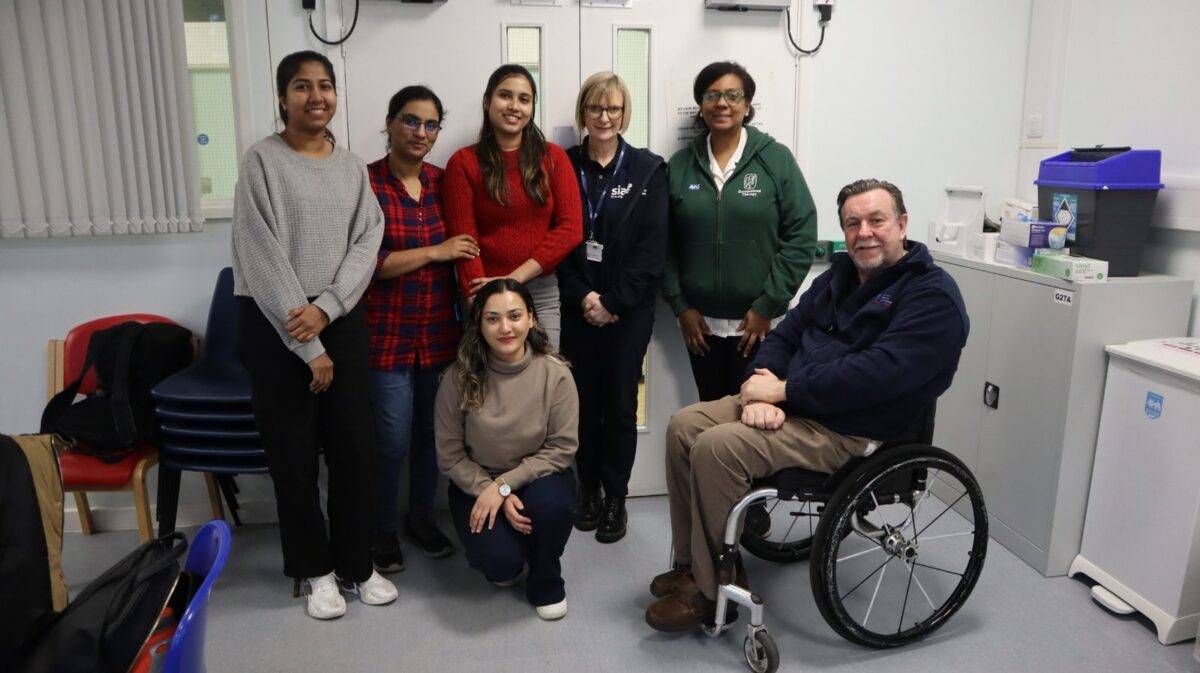 Frank Williams Academy Training team - in a clinical setting seven members of the team are seen looking at the camera one of the team on the right is in a wheelchair