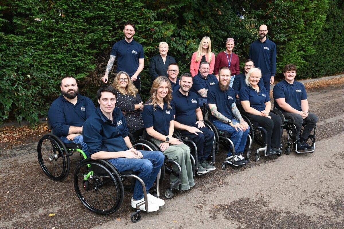 SIA Services team - a photo of 15 people outside in SIA uniforms, the front row and second row are people in wheelchairs with the back row made up of standing members of the team.
