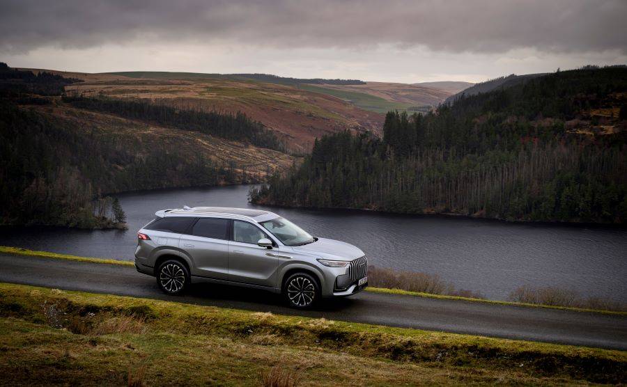 Silver JAECOO 8 driving through scottish roads beside a like and mountains