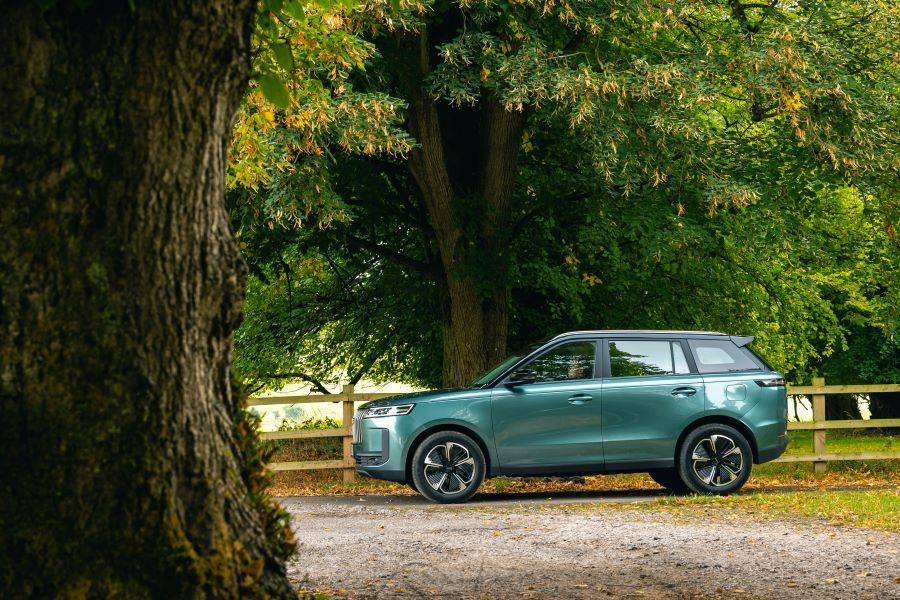 Side shot of teal colour JAECOO 5 parked in a country park with trees